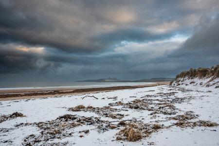 Beautiful unusual moody Winter landscape of snow on Embleton Bay beach in Northumberland Englandの写真素材