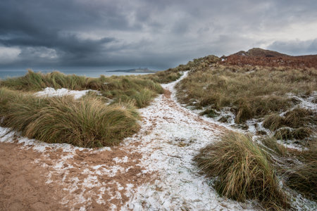 Beautiful unusual moody Winter landscape of snow on Embleton Bay beach in Northumberland Englandの写真素材