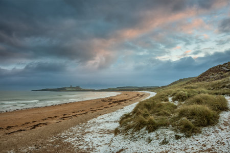 Beautiful unusual moody Winter landscape of snow on Embleton Bay beach in Northumberland Englandの写真素材