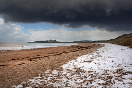 Beautiful unusual moody Winter landscape of snow on Embleton Bay beach in Northumberland Englandの写真素材