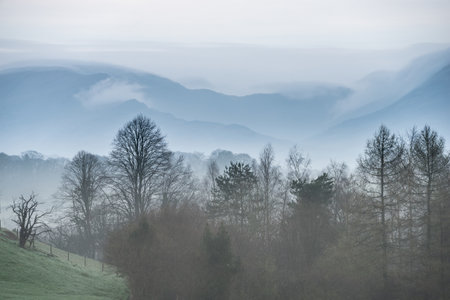 Beautiful layered landscape image of misty Spring morning in Lake District looking towards distant misty peaksの写真素材