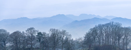 Stunning peaceful landscape image of misty Spring morning over Windermere in Lake District with boats moored on lake and distant misty peaksの写真素材