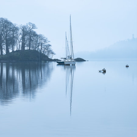 Stunning peaceful landscape image of misty Spring morning over Windermere in Lake District with boats moored on lake and distant misty peaksの写真素材