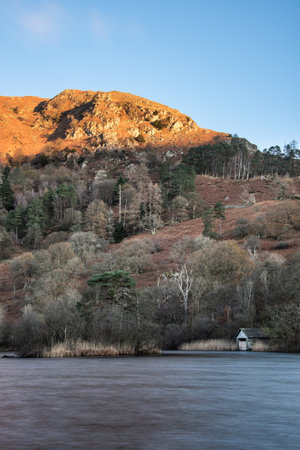 Autumn landscape sunrise image of Rydal Water boathouse in Lake District with sunlight kissing the treetopsの写真素材