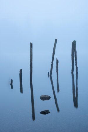 Artistic fine art Autumn foggy landscape image of wooden posts in Derwentwaterの写真素材