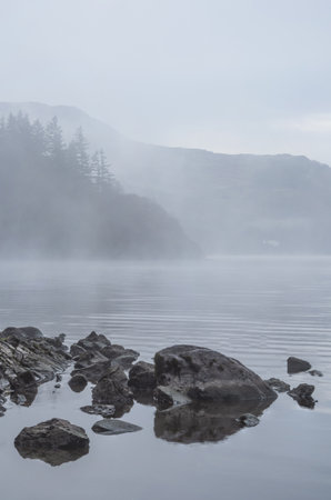 Absolutely stunning atmospheric landscape image of Derwentwater during foggy sunrise in Autumnの写真素材