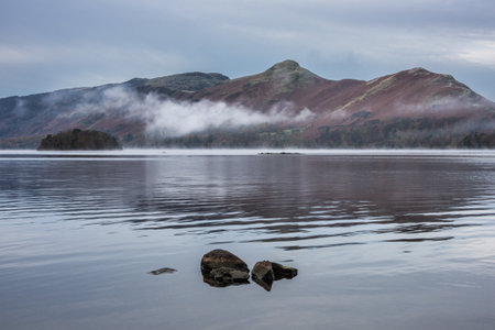 Absolutely stunning atmospheric landscape image of Derwentwater during foggy sunrise in Autumnの写真素材
