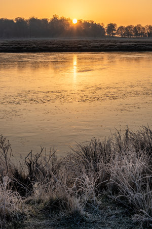 Beautiful Winter sunrise landscape image of frozen fields and grasses with sun glow on the frosty groundの写真素材
