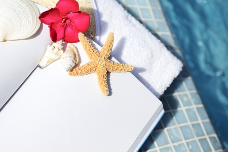 open book, shellfish and white towel beside a poolの写真素材
