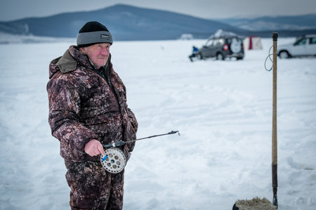 Baikal lake, Siberia, Russia - March 05, 2020 : Winter ice fishing. A fisherman is fishing on spinings near tents and cars on Lake Baikal on a March day. Baikal lake, Siberia, Russiaのeditorial素材