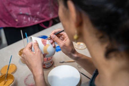 women's hands painting a pottery object