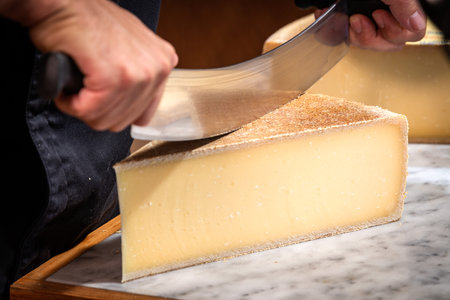 A man cuts a portion of The GruyÃ¨re with a wire, the famous swiss cheese in a cellar on a marble backgroundの写真素材