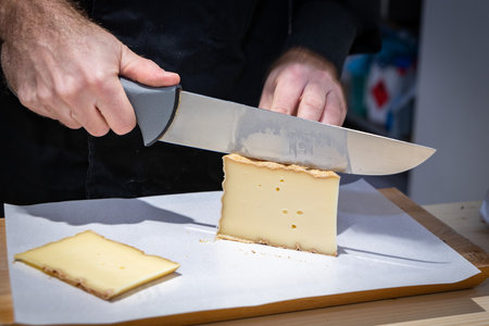 July 11 2022, Lyon, France: A man cuts a portion of The Vacherin Fribourgeois with a wire, a famous swiss cheeseの写真素材