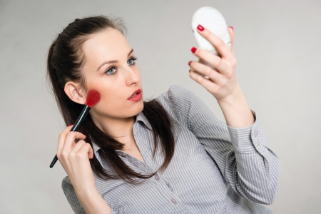 Portrait of a young woman applying make up, grey backgroundの写真素材