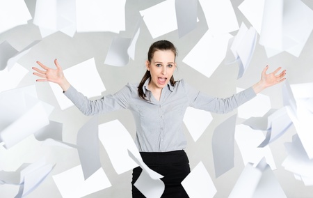 Frustrated young businesswoman with falling paper documents, gray background 