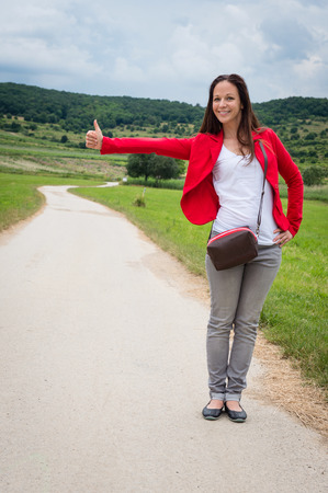 Portrait of young lady in red jacket hitchhiking by the roadの写真素材