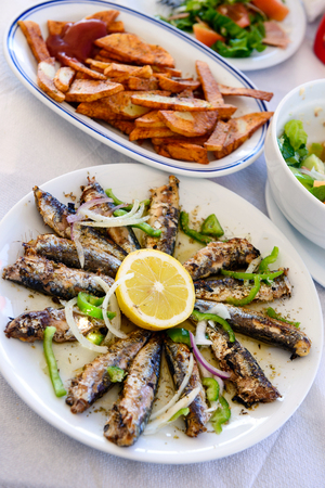 Freshly grilled sardines on a plate with lemon and fried potatoesの写真素材