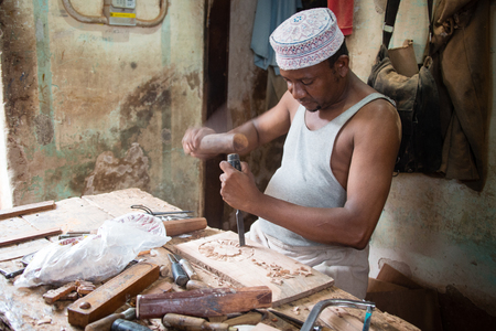 STONETOWN, ZANZIBAR - JAN 1, 2018: Carpenter creating ornaments on wooden board using traditional manual tools in Stonetown, Zanzibarのeditorial素材