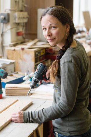 Young woman using a electric screwdriver on a piece of wood at workshop