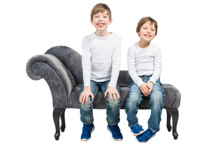 Portrait of two young boys with their mouth open, sitting on a couch, isolated on white backgroundの写真素材