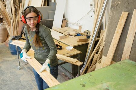 Young woman processing wooden plank at workshop