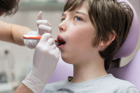 Dentist demonstrating young boy how to brush teeth in dental clinicの写真素材