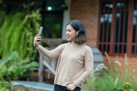 Asian girl relax in the garden with her cell phone and face time with her friendの写真素材