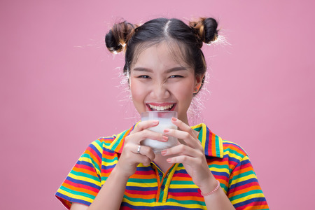 Young pretty asian girl drinking milk on pink background