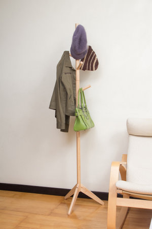 Wooden coat rack with jacket, hats and handbag in the room background
