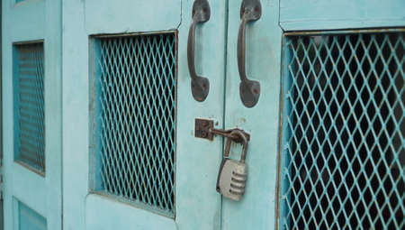 Vintage blue wooden folding door with metal rusted latch and unlocked padlockの写真素材
