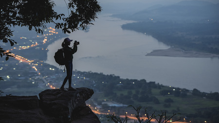 Woman standing on a cliff with the river below,Woman standing on cliff in front of a  mountain and river view around.の写真素材