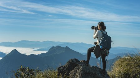 the tourist standing on cliff in front of a sunset and  taking pictures of fog in mountain view around.View of mountains, winter landscape with foggy hills at sunrise.の写真素材