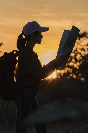 Traveler searching right direction on map,freedom lifestyle concept at sunset light,traveller with backpacks relaxing on top of a mountain at sunset,traveler with backpack,Lifestyle concept adventureの写真素材