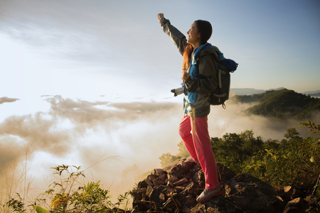 The adventurer stands at the top of the mountain with foggy morning sky with the shadow of a distant mountain,freedom lifestyle concept traveller with backpacks relaxing.の写真素材