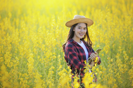 Vietnamese girl with yellow flowers.Beautiful Happy Smiling Young Asian Woman Wearing Traditional White Ao Dai Dress(Clothing), Vietnamese Conical Hat Leaf Hat In Flower Garden.の写真素材