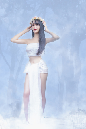 Beautiful young girl in white dress. Flowing fabric. Petty girl in white dress with foggy on a winter. Fashion Model Beauty Dress, Waving White Cloth Gown, Woman in White Fluttering Clothes Fabric.の写真素材