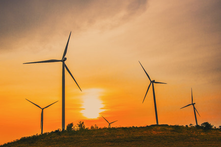 Windmills for electric power production surrounded by mountain. Wind turbine for electric power production with blue sky. Beautiful sunset above the windmills on the field.の写真素材