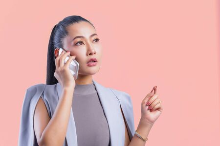 Woman working on laptop at office while talking on phone, Portrait of confident young woman working in her office with mobile phone. Working woman with colorful background.の写真素材