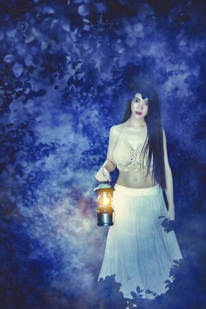 Cute Asian girl wearing a white dress in a mysterious forest. Beautiful girl with lanterns in the forest.の写真素材