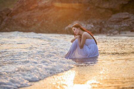 Beautiful young women are enjoying the beach side relaxation.A beautiful young girl enjoys the sea with waves and soft sunlight at sunset.の写真素材