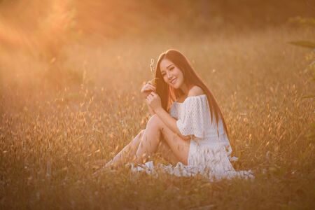 Beautiful woman wearing a white dress, happy with the meadow and sunset.の写真素材