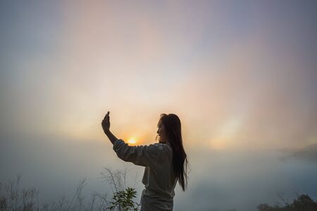 Tourists with fog on the top of the hill. Travelers breathe fresh air while photographing the beautiful sunrise and mist.の写真素材