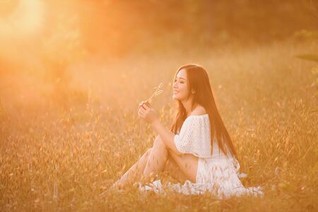 Beautiful woman wearing a white dress, happy with the meadow and sunset.の写真素材