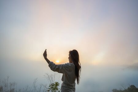 Tourists with fog on the top of the hill. Travelers breathe fresh air while photographing the beautiful sunrise and mist.の写真素材