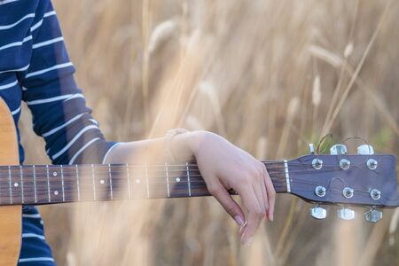 Guitar in the grass. Close up of a hand with a guitar in a brown meadow background.の写真素材