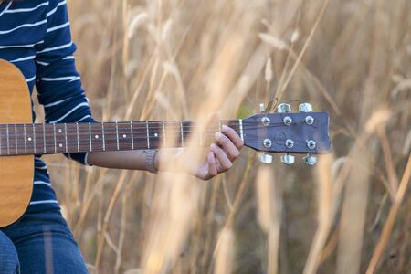 Guitar in the grass. Close up of a hand with a guitar in a brown meadow background.の写真素材