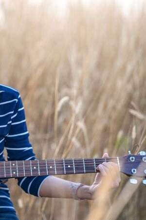 Guitar in the grass. Close up of a hand with a guitar in a brown meadow background.の写真素材