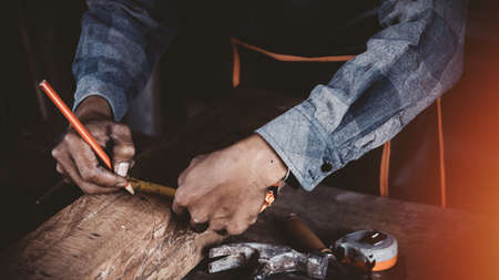 Carpenter working on woodworking machines in carpentry shop. Carpenter marks out the details of the furniture cabinet using a set square close up view.の写真素材
