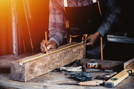 Carpenter working on woodworking machines in carpentry shop. Carpenter marks out the details of the furniture cabinet using a set square close up view.の写真素材