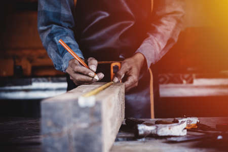 Carpenter working on woodworking machines in carpentry shop. Carpenter marks out the details of the furniture cabinet using a set square close up view.の写真素材